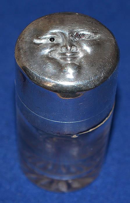 SILVER TOP GLASS BOTTLE WITH GROTESQUE FACE ON LID.